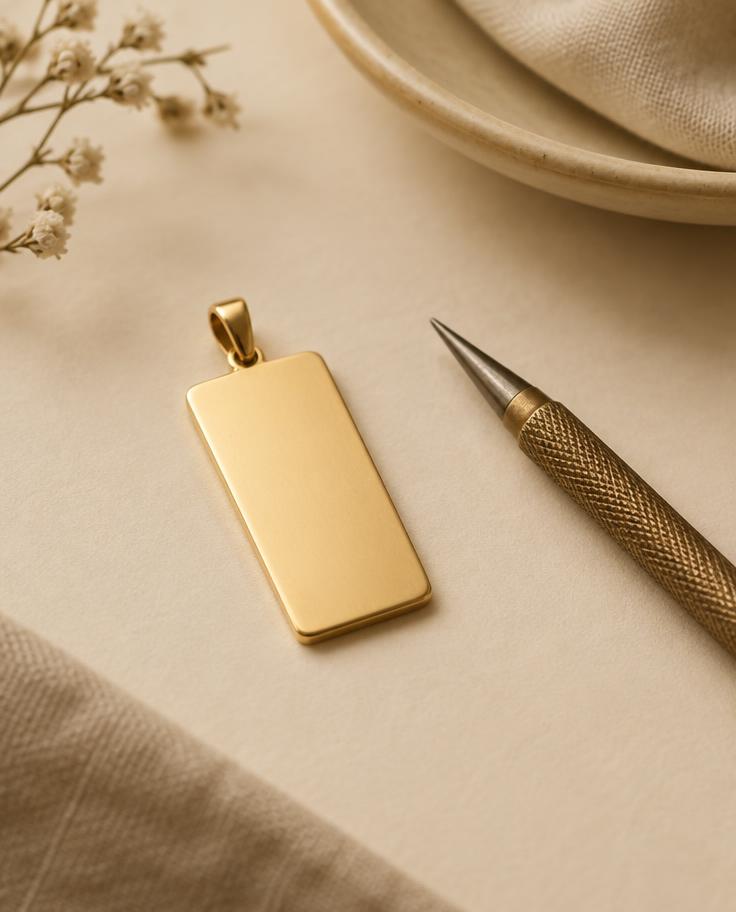 Blank gold engravable pendant beside an engraving tool